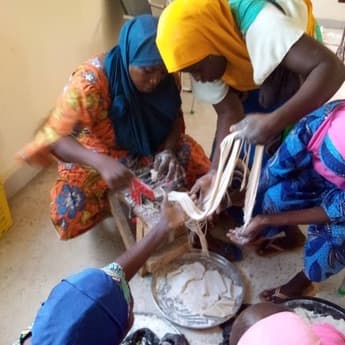 Four women working together over a bowl and pestle, processing raw material during a hands-on training session.